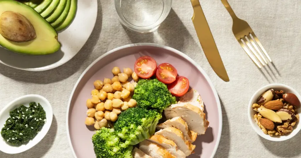 Imagen en la que podemos ver un plato de comida: garbanzos, tomate, pollo y con una gran cantidad de brócoli.