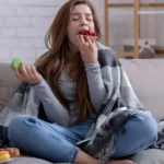 Persona comiendo de forma descontrolada en el sofá para demostrar la relación entre la ansiedad y alimentación.