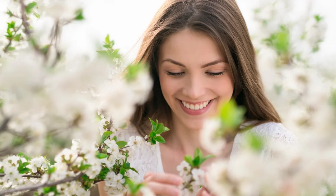 Mujer sonriente entre flores blancas de cerezo durante la primavera.