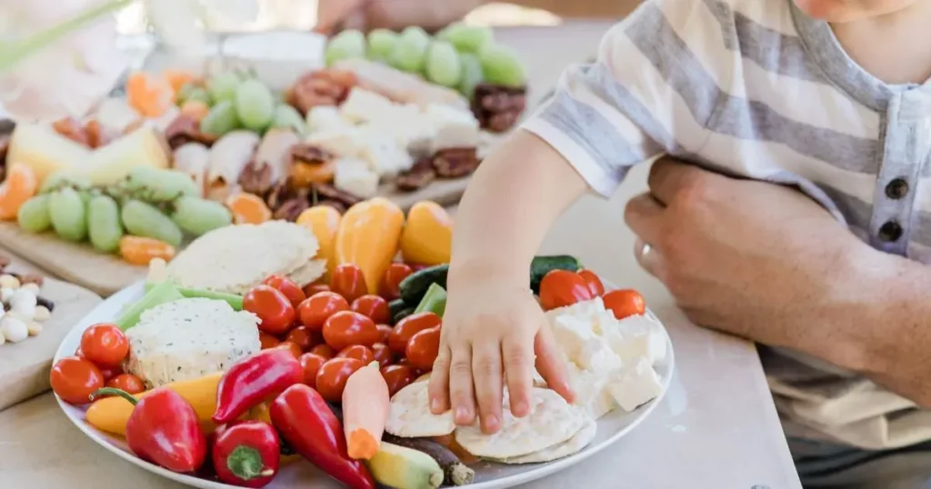 Un niño cogiendo verduras de un plato mientras lo sostiene su padre.