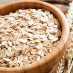 Tarro de madera con copos de avena y gramíneas al lado.