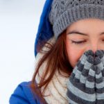 Chica tapándose la nariz con guantes tras echarse crema de manos natural para proteger las manos del frío.