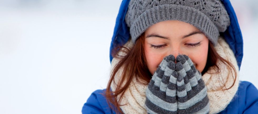 Chica tapándose la nariz con guantes tras echarse crema de manos natural para proteger las manos del frío.