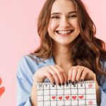 Joven con un calendario de frutas y verduras de temporada en la mano y una cesta de fruta al costado.