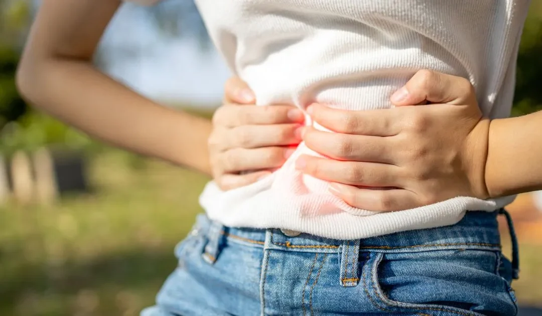 Mujer con molestias estomacales y manos sobre la barriga.