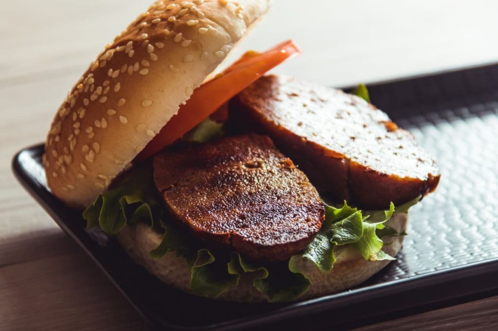 Plato de seitán en formato hamburguesa y salsa barbacoa.