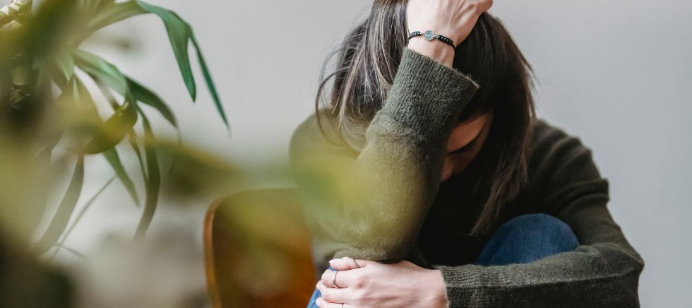 Mujer con una mano en la cabeza y otra abrazándose sufriendo los síntomas del trastorno de ansiedad generalizada.